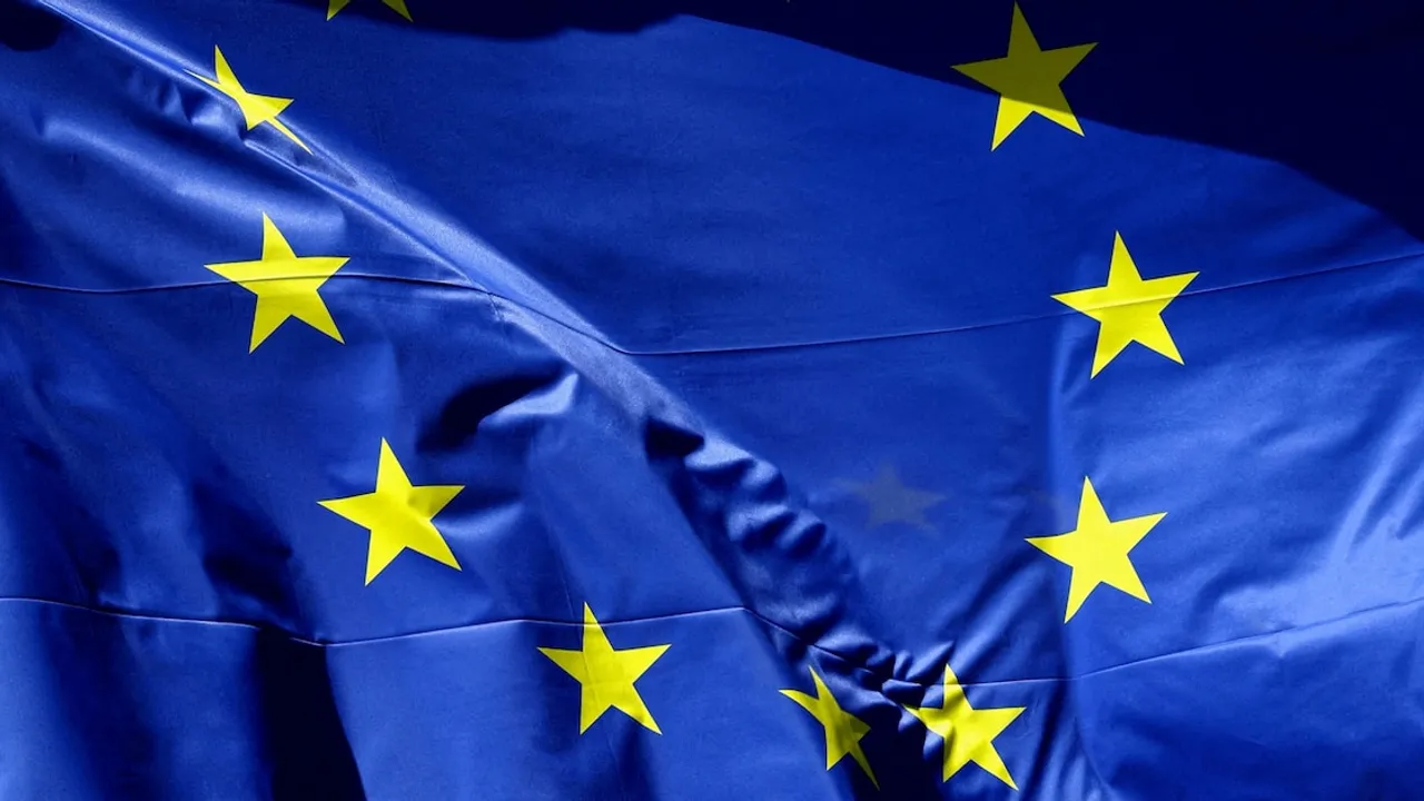 Bandera azul de la Unión Europea con doce estrellas doradas en círculo ondeando con pliegues sobre fondo oscuro.