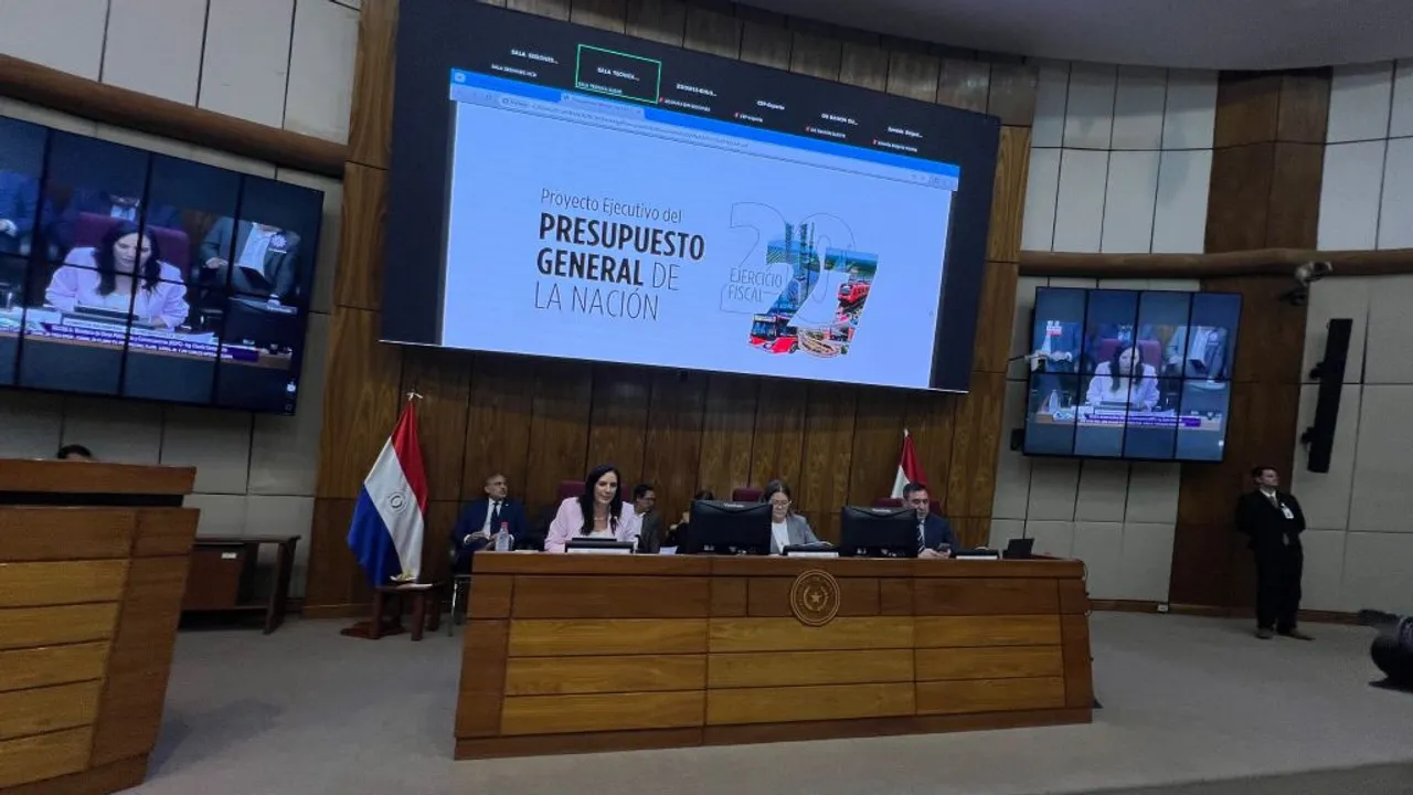Autoridades sentadas en la mesa principal de una sala parlamentaria frente a una pantalla de presentación del presupuesto