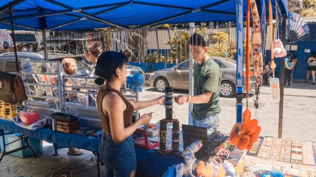 Joven atiende a una clienta frente a un mostrador de pulseras bajo un toldo azul en un puesto callejero