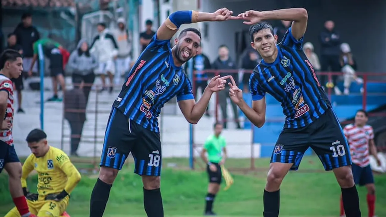 Dos futbolistas con camiseta a rayas azul y negro celebran juntos en la cancha formando un arco con los brazos