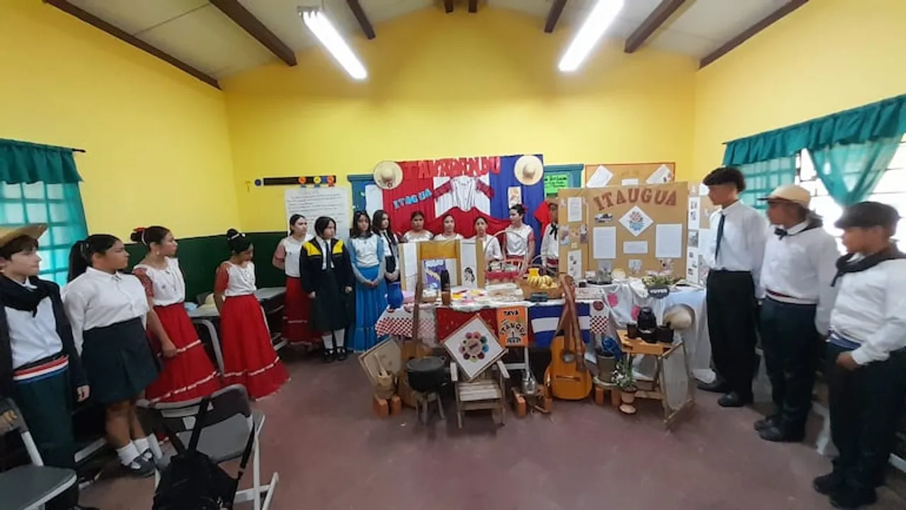 Estudiantes vestidos con trajes tradicionales y uniformes escolares exponen proyectos culturales en un aula.