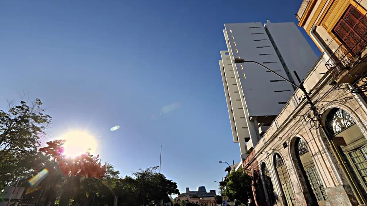 Edificios urbanos y árboles bajo un cielo despejado e iluminado por el sol matutino en Asunción.
