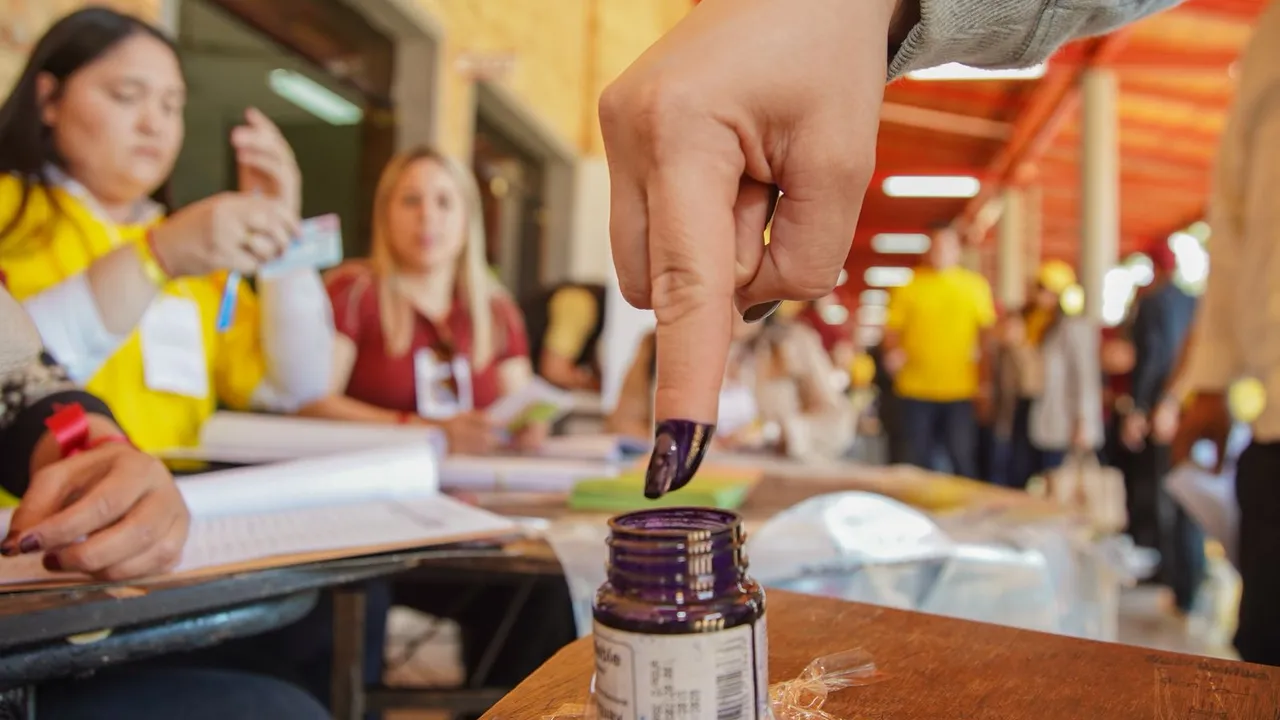 Dedo índice de un elector entintado con tinta indeleble frente a una mesa de votación en una jornada cívica.