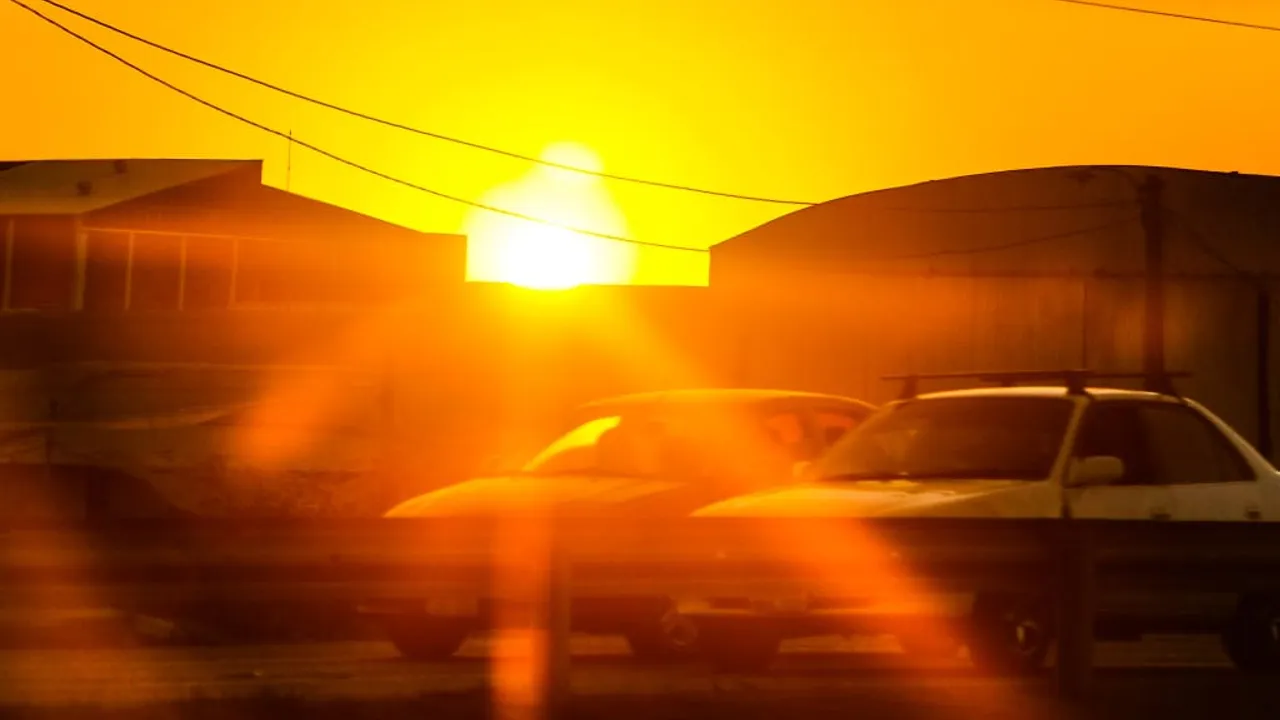 Sol brillante en el horizonte urbano entre edificios y vehículos estacionados a plena luz del día