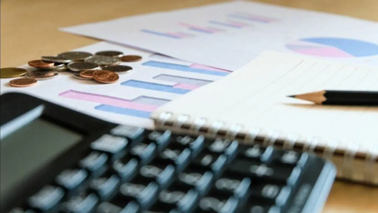 Calculadora, libreta con lápiz, monedas y hojas con gráficos financieros impresos sobre una mesa de madera.