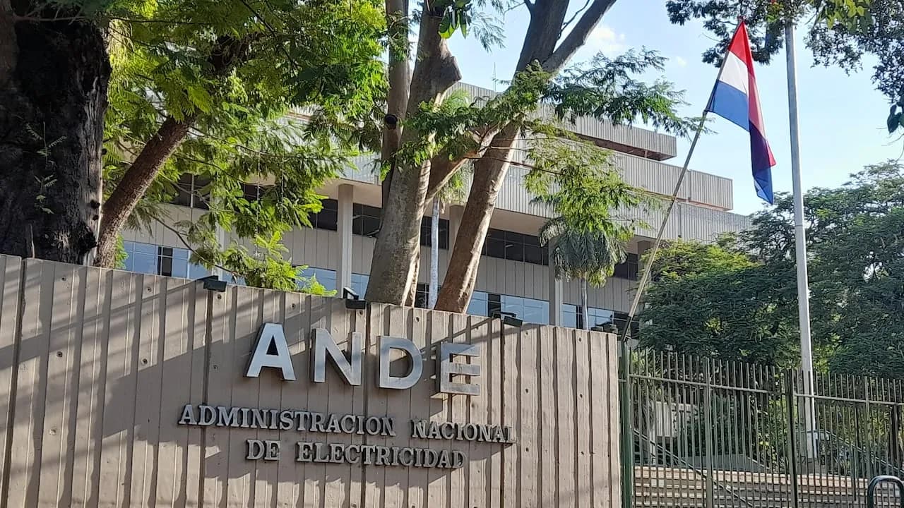 Fachada de la sede central de la ANDE con letras metálicas, rejas y la bandera paraguaya izada.