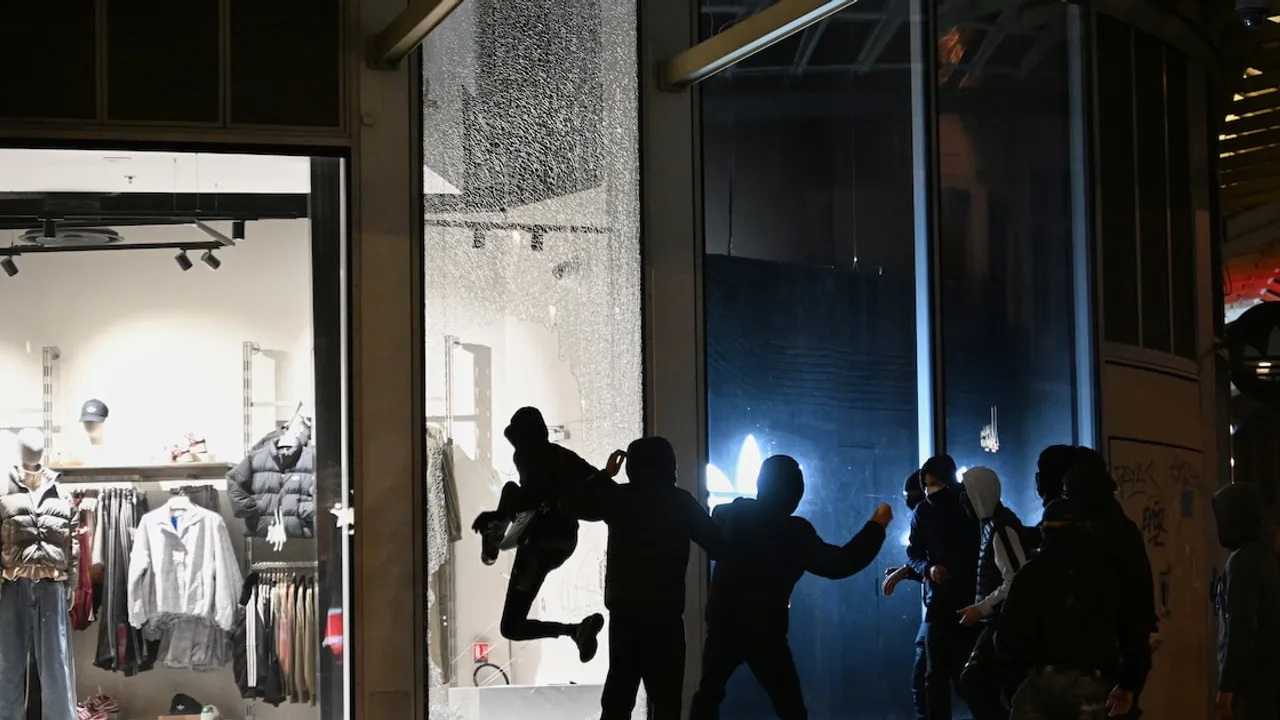 Jóvenes con el rostro cubierto rompen la vidriera de un comercio durante disturbios nocturnos.