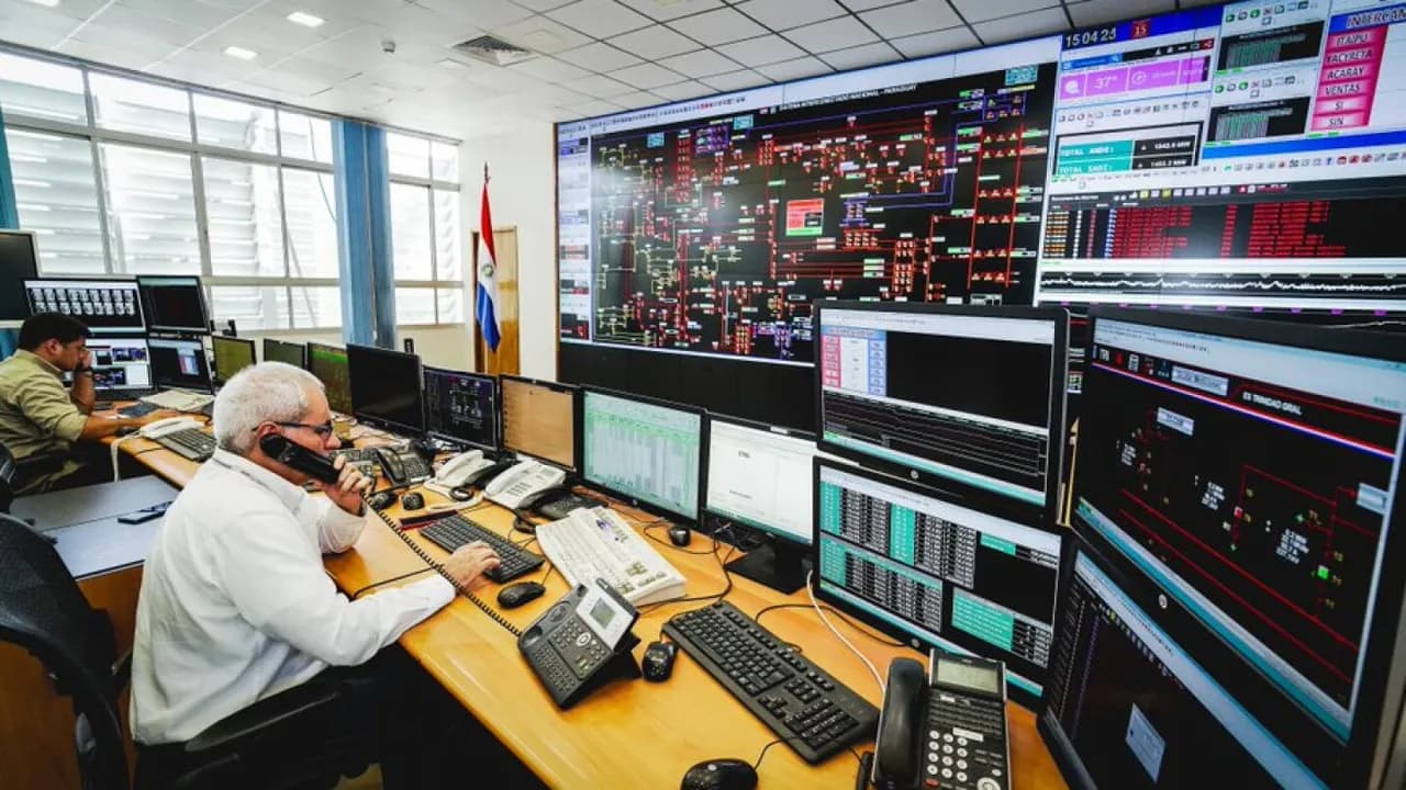Técnicos de la ANDE operan computadoras y atienden teléfonos frente a una gran pantalla del sistema eléctrico.