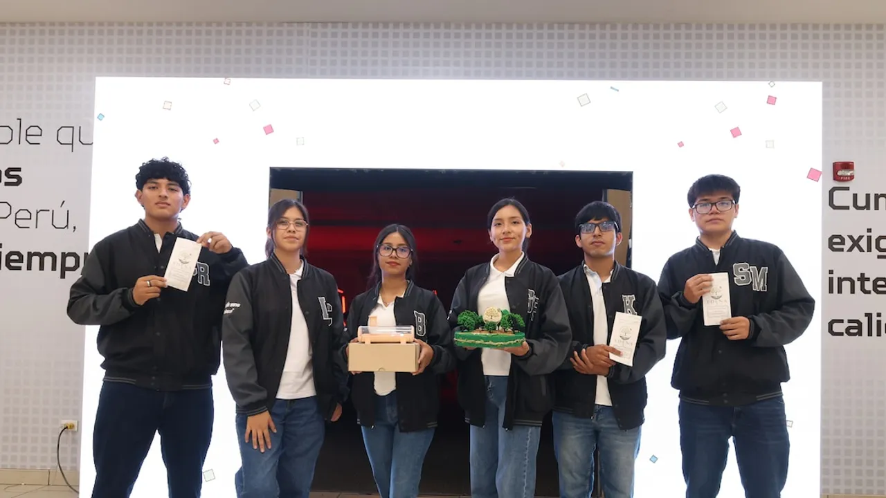 Seis estudiantes con camperas oscuras posan sosteniendo maquetas, folletos y prototipos ecológicos en un auditorio.