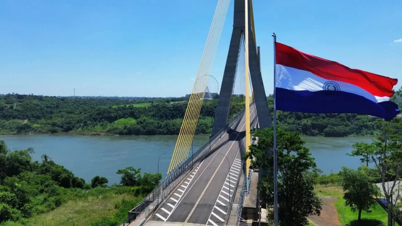 Puente atirantado sobre el río Paraná con la bandera paraguaya flameando en primer plano en un día despejado.