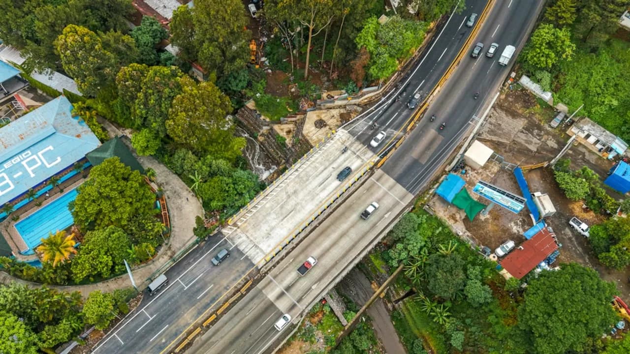Vista aérea de un puente vehicular de concreto rodeado de vegetación con automóviles en circulación.