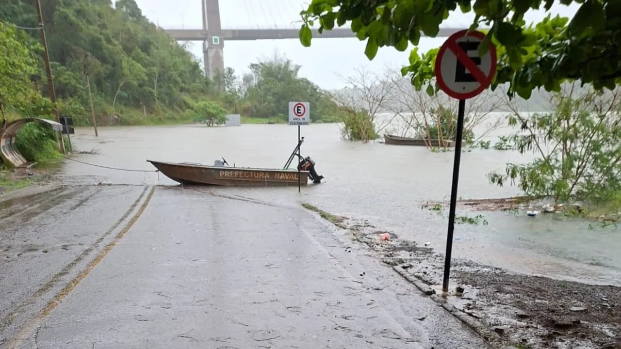 Rampa costera inundada con un bote de la Prefectura Naval amarrado y señales de tránsito bajo la lluvia.