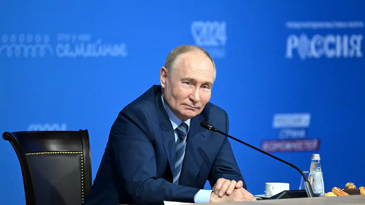 Vladimir Putin sentado frente a un micrófono en una conferencia sobre fondo azul en un acto oficial.