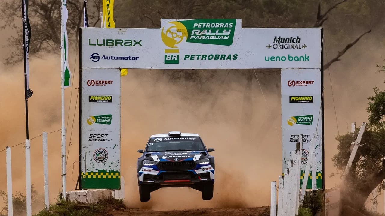 Auto de carreras en pleno salto bajo un arco de llegada sobre un camino de tierra durante una prueba deportiva.