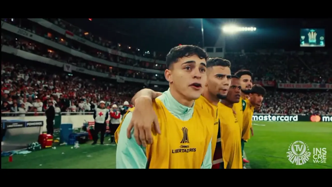 Futbolistas con chaleco amarillo abrazados al borde del campo de juego en un estadio nocturno iluminado.
