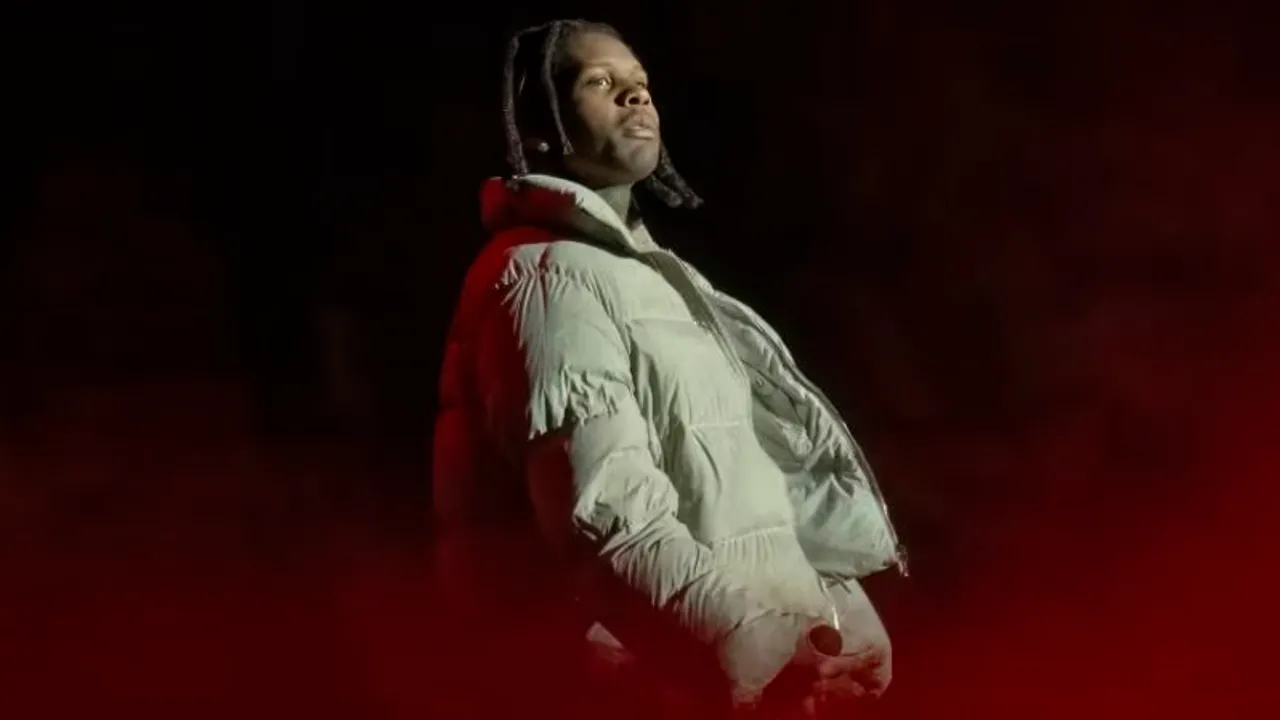 El rapero Lil Durk de perfil sobre un escenario con iluminación roja de fondo vistiendo una campera inflable clara.