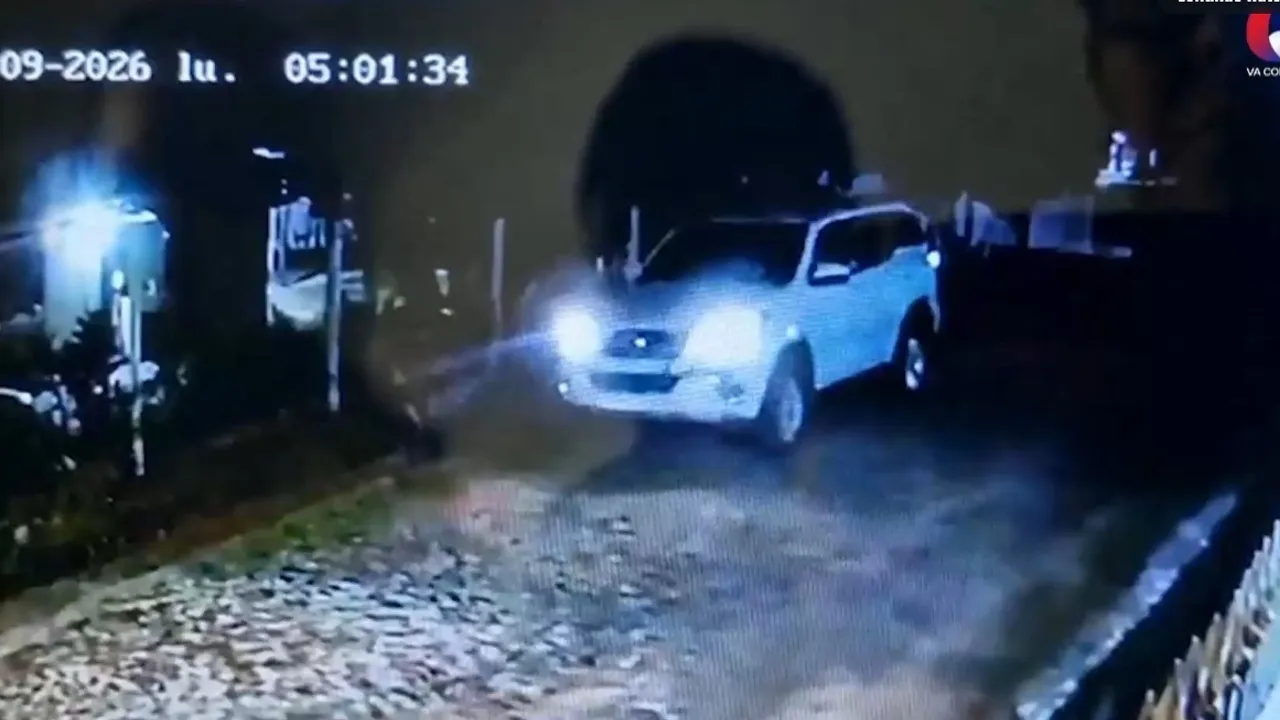 Camioneta blanca transita de noche con luces encendidas por calle empedrada en toma de seguridad.