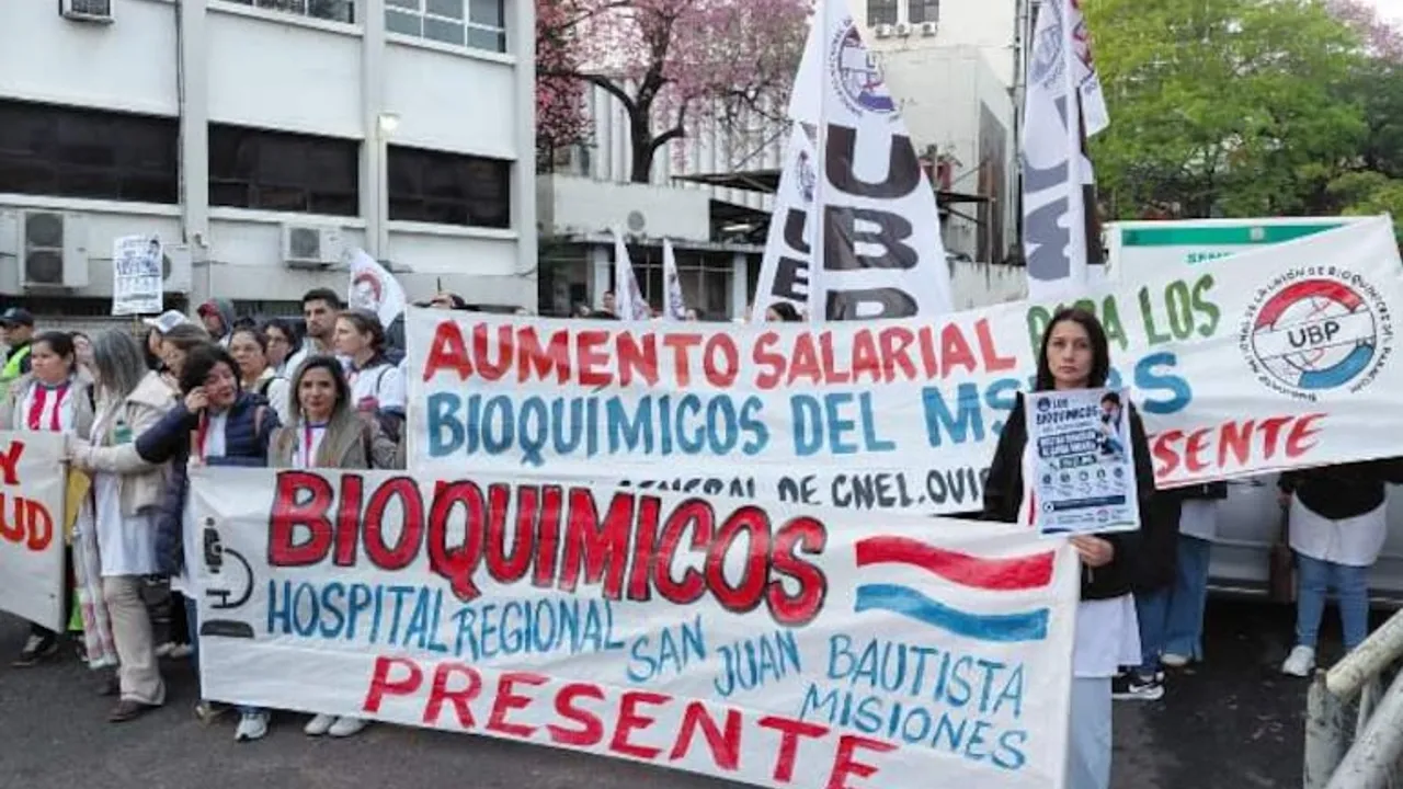 Manifestantes sostienen pancartas y banderas frente a un edificio público exigiendo aumento salarial.