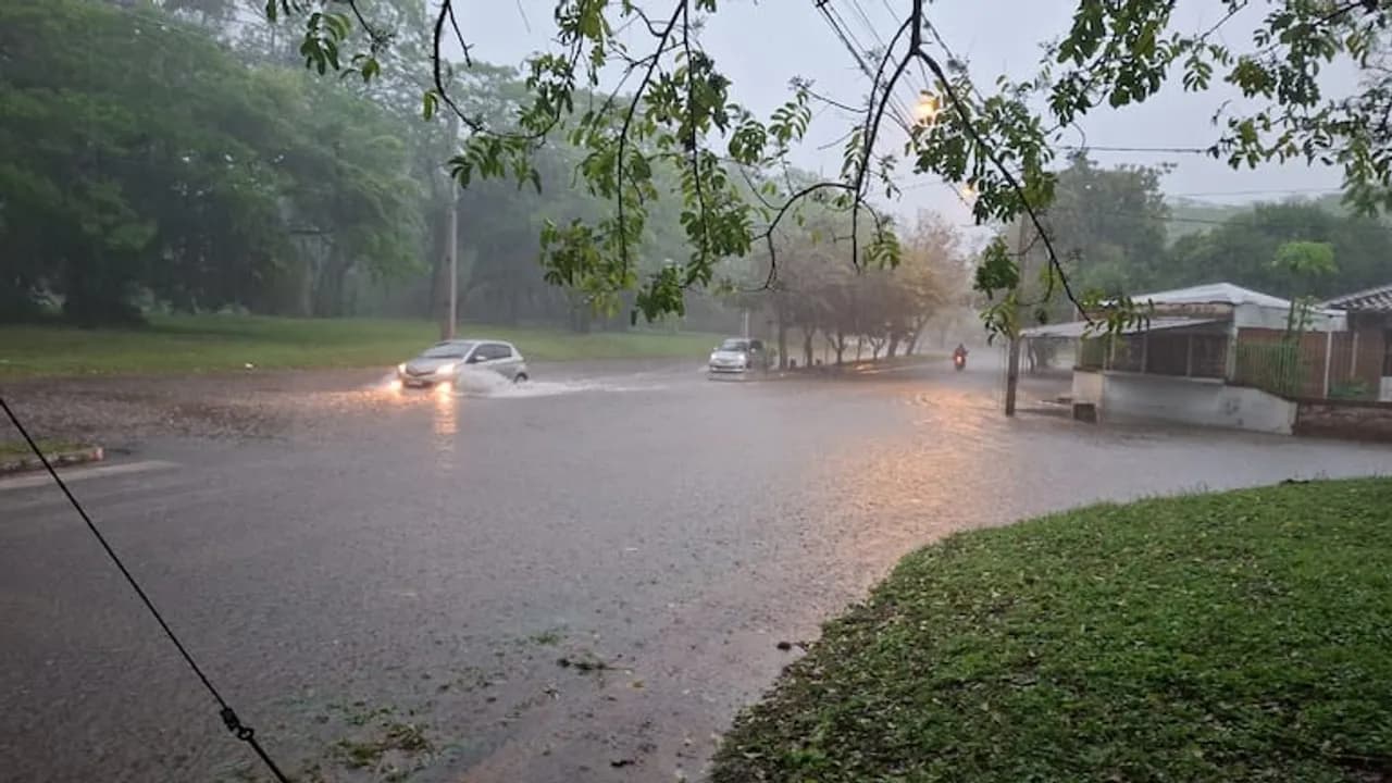 Vehículos circulan con luces encendidas por una avenida anegada de agua durante una intensa lluvia diurna.