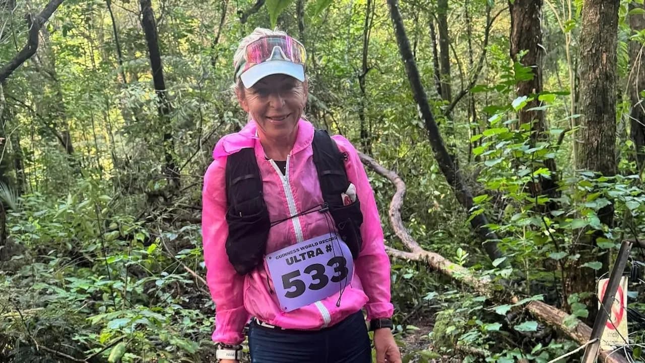Corredora con campera fucsia, chaleco de hidratación con dorsal 533 y visera en medio de un sendero boscoso.