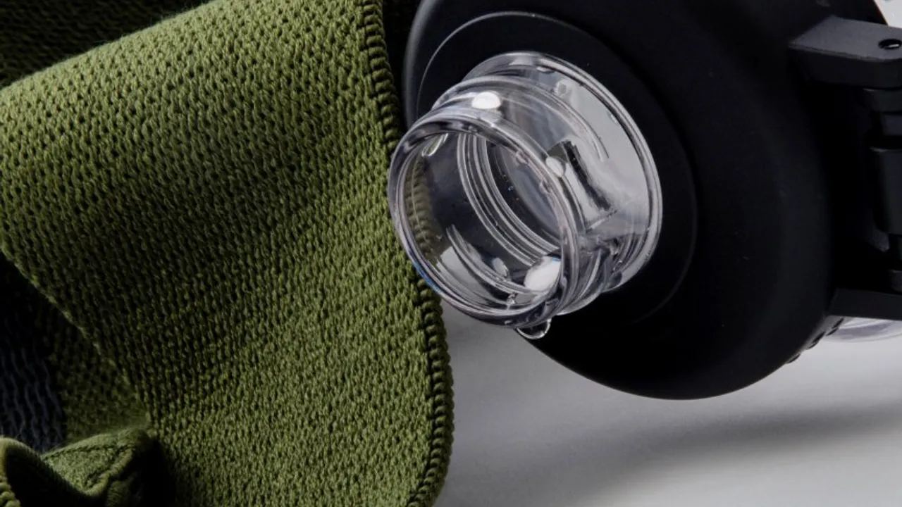 Detalle de la boquilla de una botella transparente con una gota de agua junto a una tela verde de entrenamiento