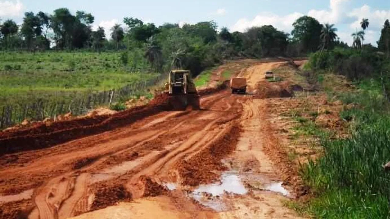 Maquinaria pesada trabajando en la nivelación de un camino de tierra roja en una zona rural con vegetación.