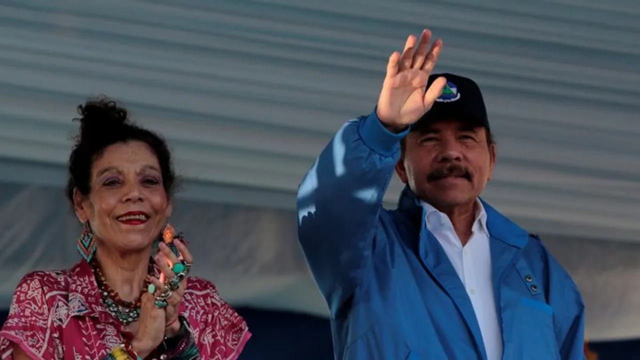 Daniel Ortega y Rosario Murillo saludan al público con la mano alzada durante un acto político al aire libre.