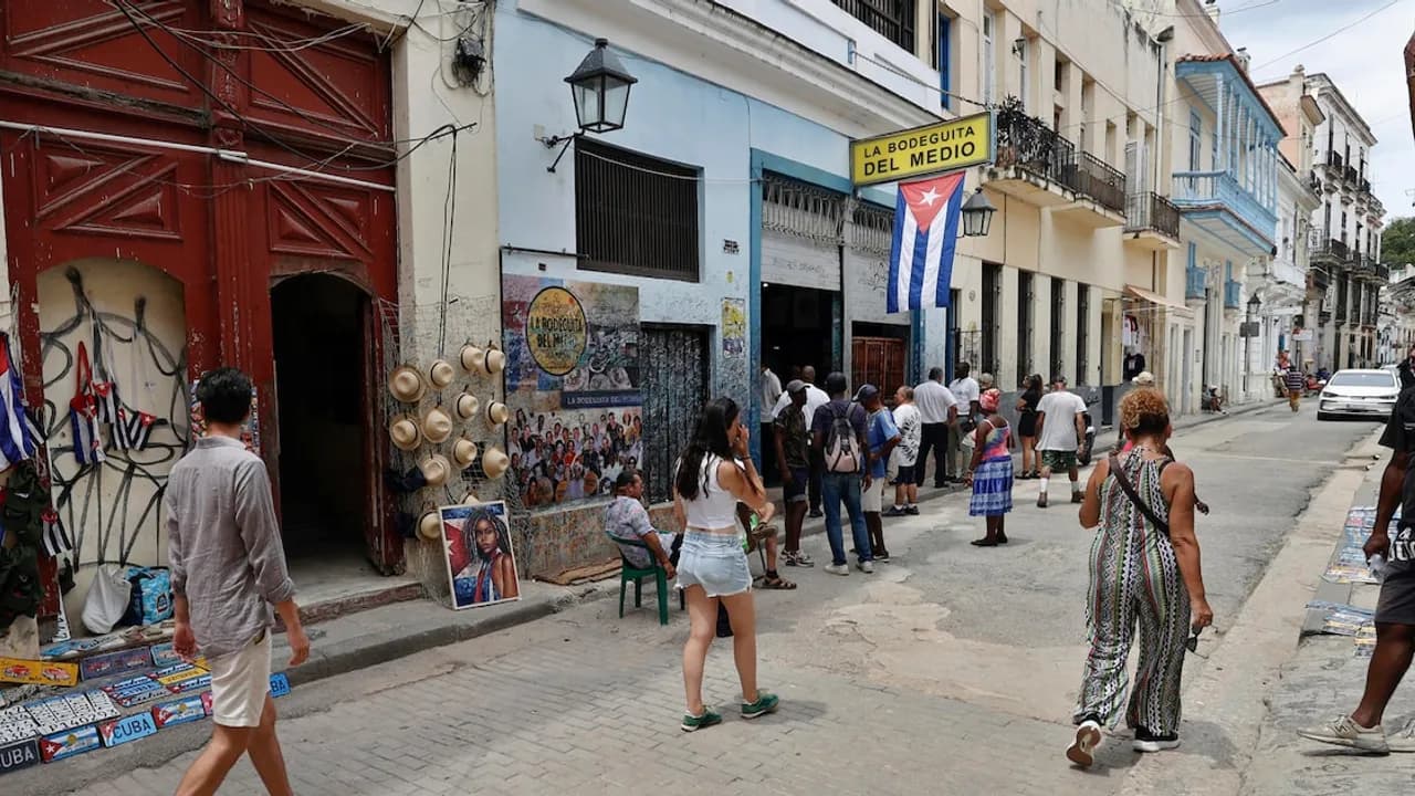 Transeúntes caminan por una calle adoquinada frente a la fachada del histórico bar La Bodeguita del Medio.