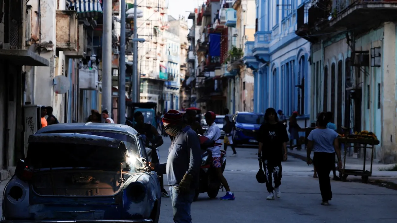 Un hombre realiza trabajos de soldadura en un automóvil antiguo sobre una calle urbana de La Habana.