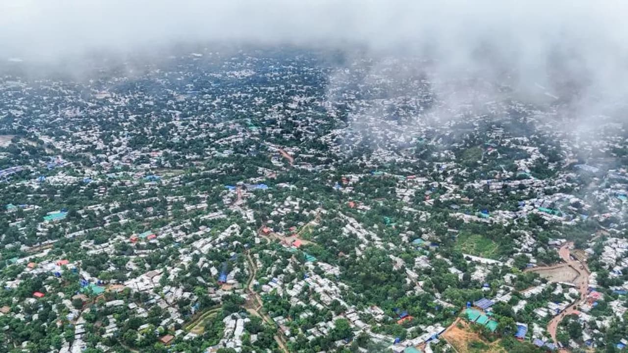 Vista aérea de un extenso campamento de refugiados con precarias viviendas entre colinas verdes bajo la niebla.