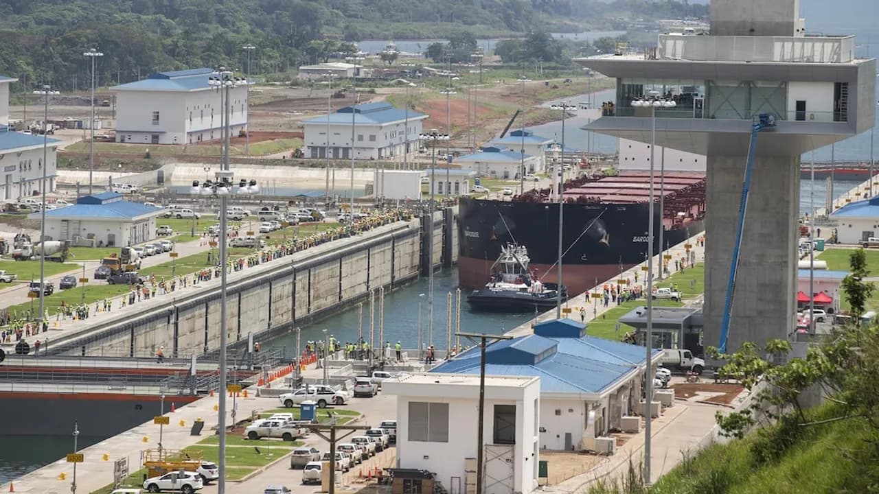 Barco de gran porte cruzando una esclusa del Canal de Panamá junto a la torre de control y operarios.