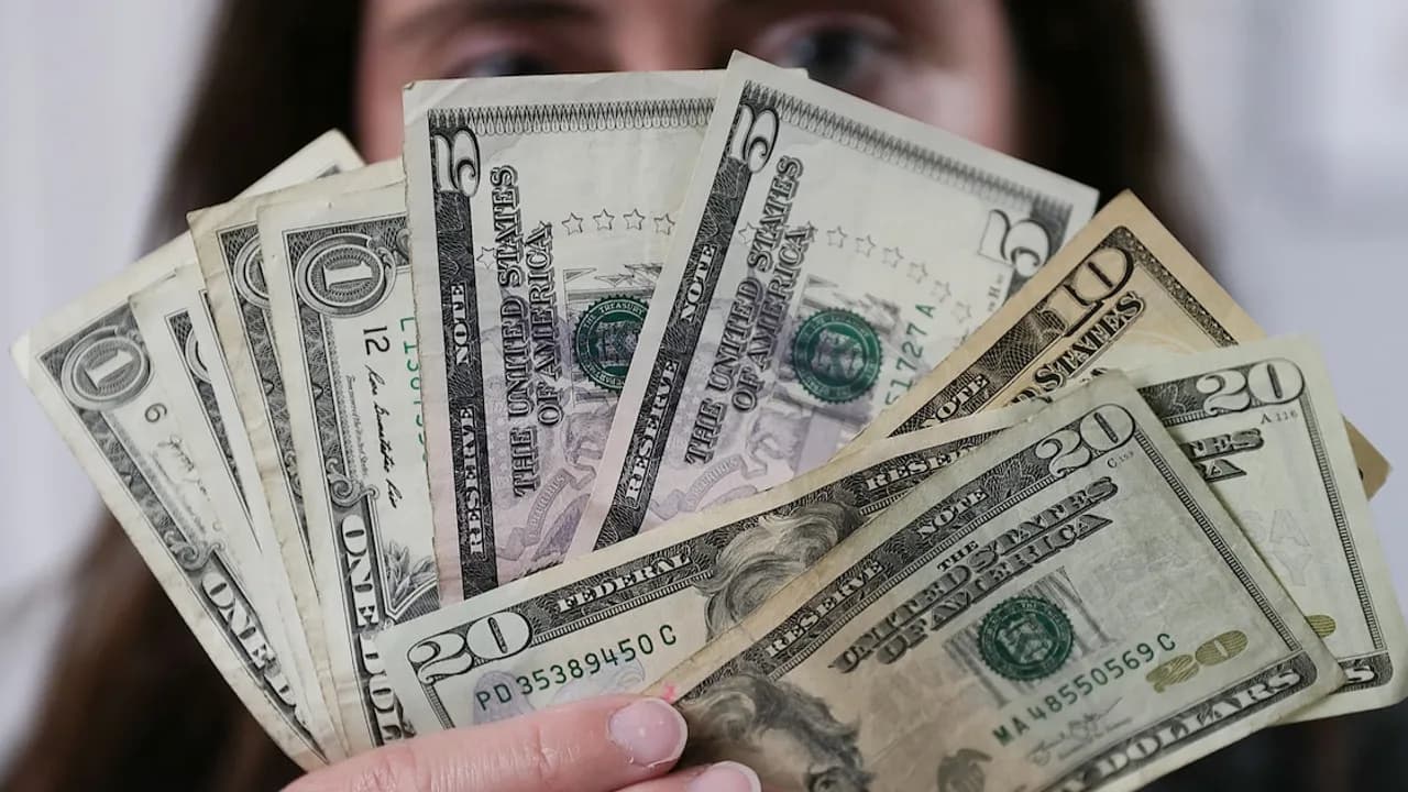 Persona sosteniendo en abanico varios billetes de dólares estadounidenses frente a su rostro.