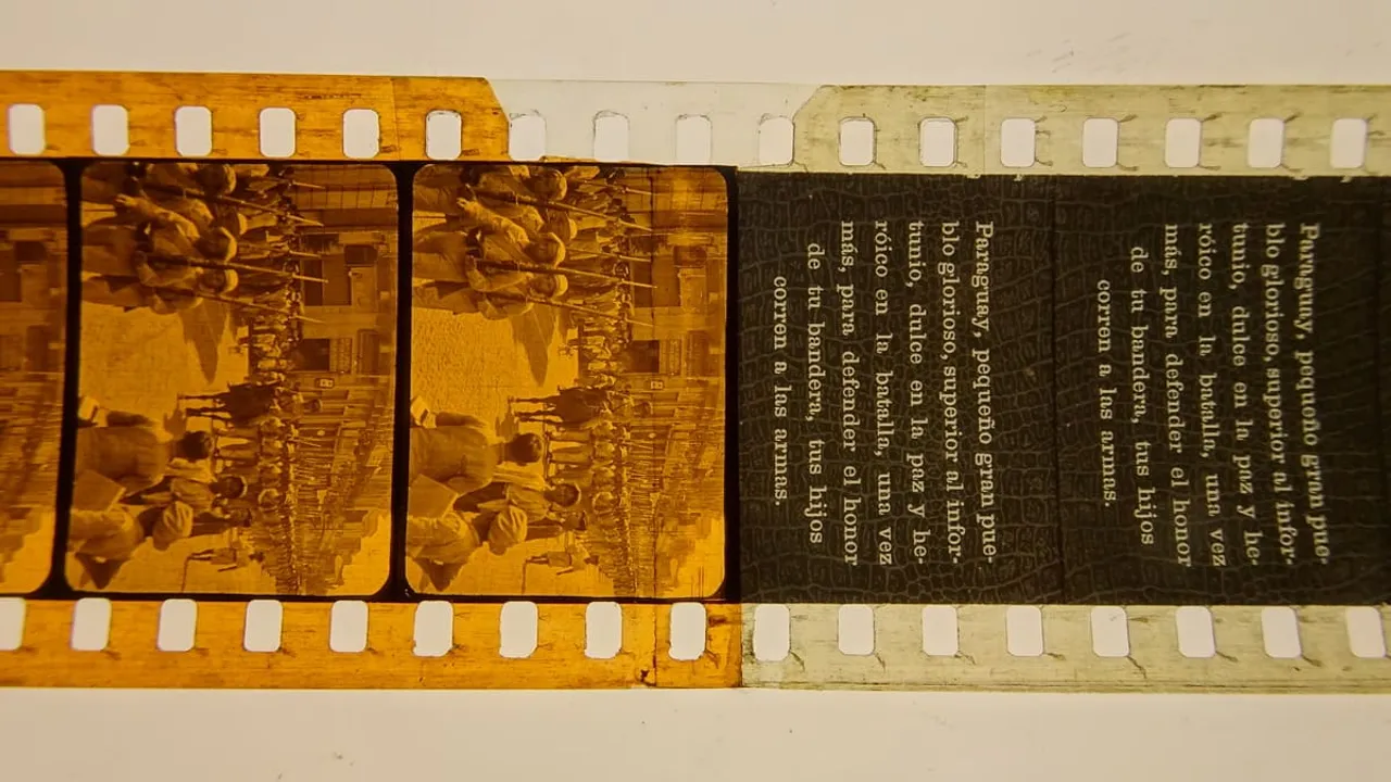 Tira de película de 35 mm con fotogramas de soldados marchando junto a una placa con texto patriótico.