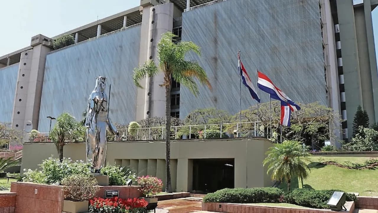 Edificio del Banco Central del Paraguay con jardines, banderas paraguayas y una estatua plateada.