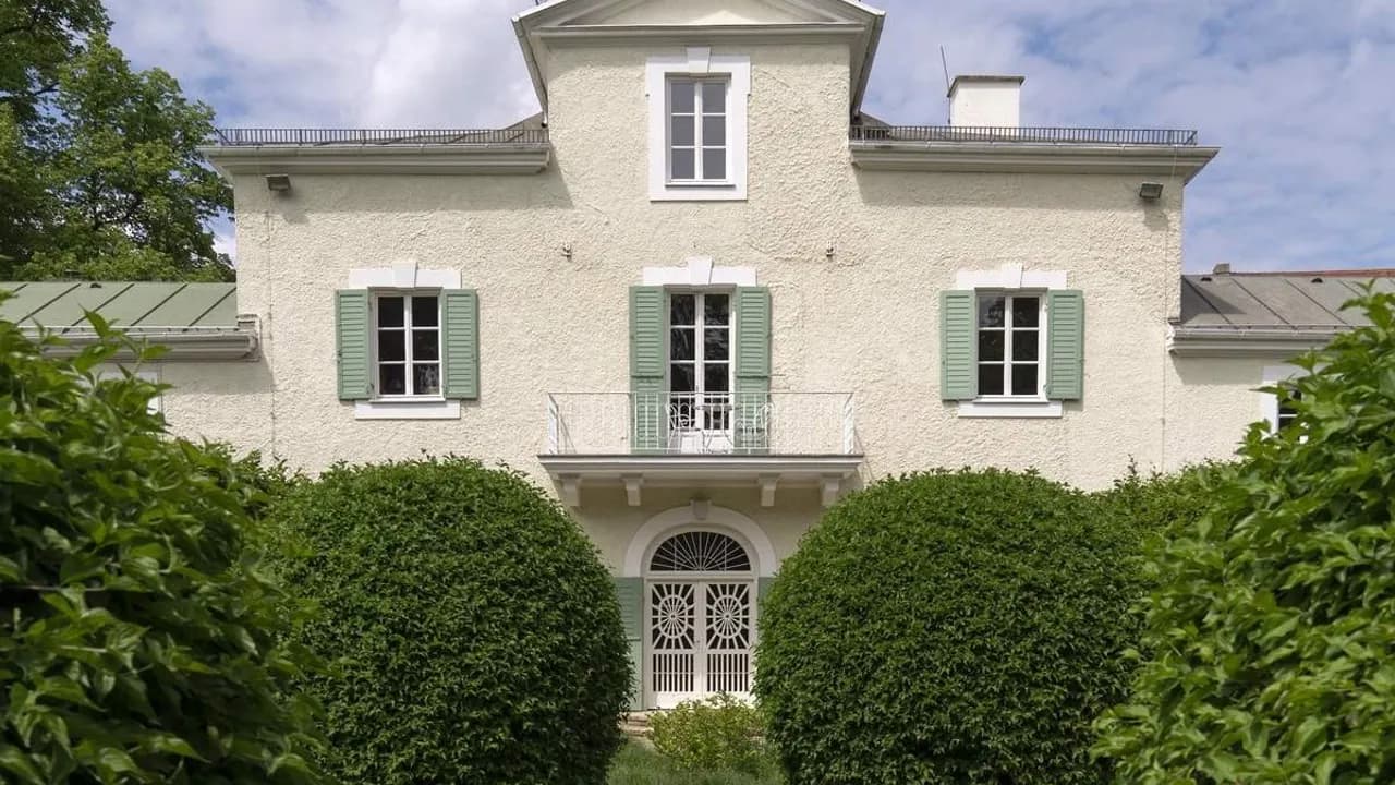 Fachada de la casona histórica Ebenböckhaus con ventanales verdes y arbustos redondeados en el jardín.