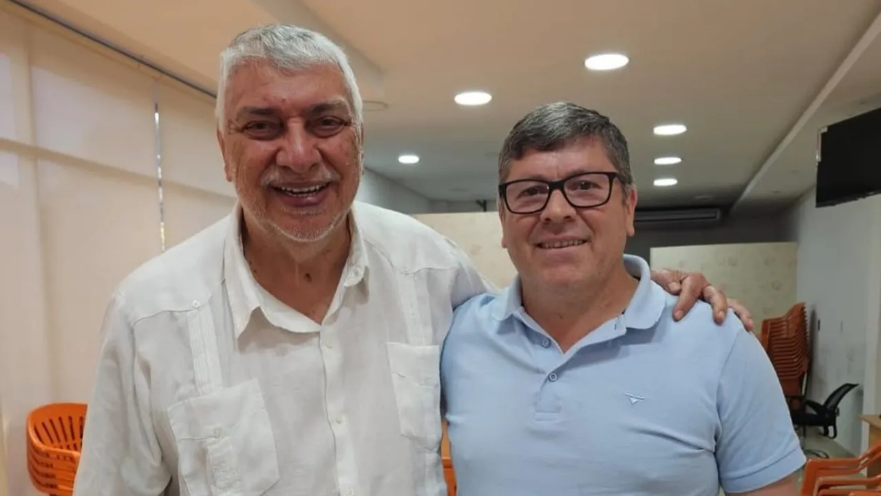 Fernando Lugo y Daniel Mujica sonríen juntos en una sala iluminada vistiendo camisas informales.