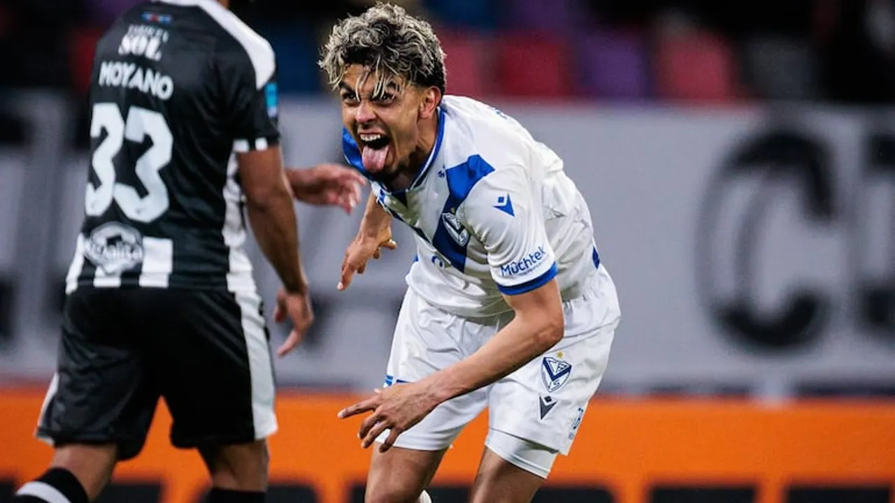 Futbolista festeja con la lengua afuera vistiendo camiseta blanca con detalles azules en un campo deportivo