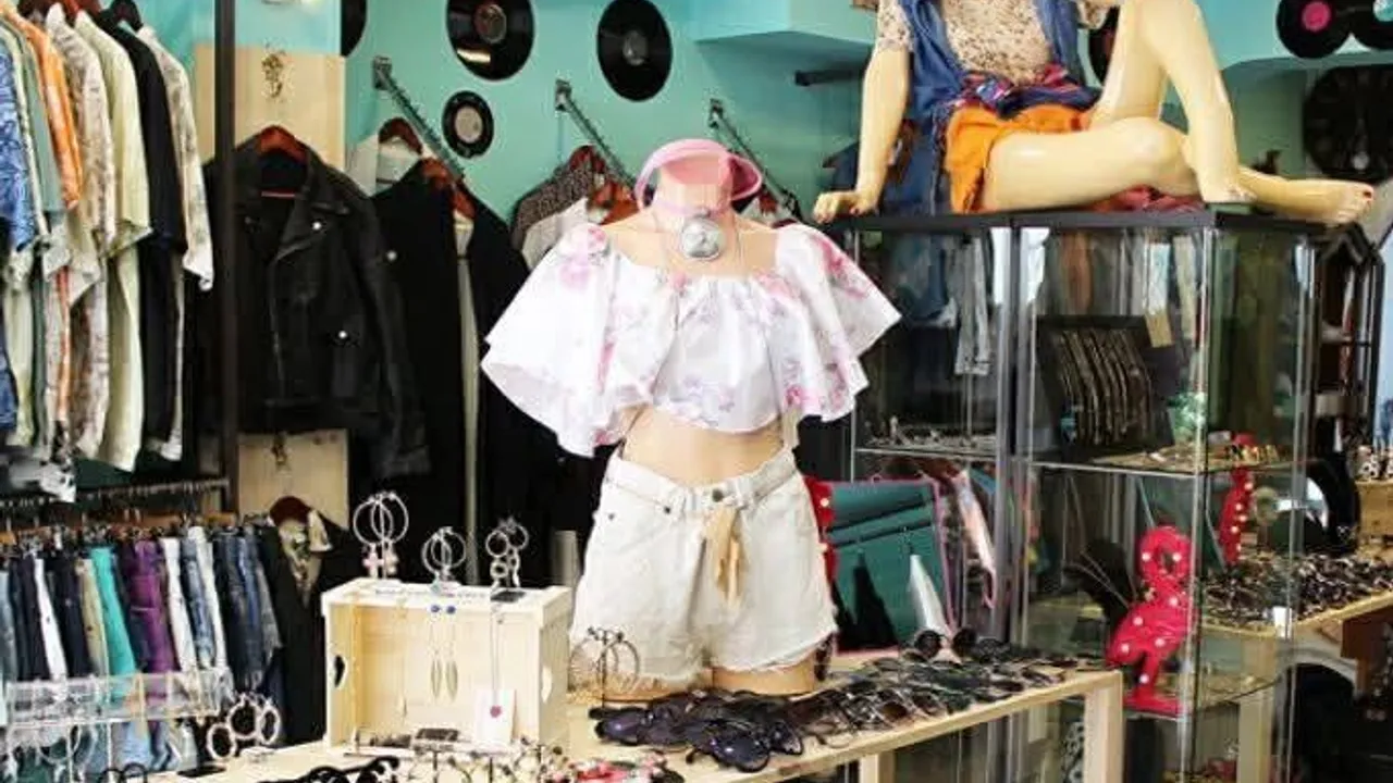Maniquíes vestidos dentro de una tienda de prendas vintage con anteojos sobre una mesa y vinilos decorativos.