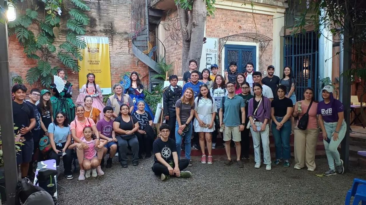 Grupo de jóvenes y adultos reunidos en el patio empedrado de un centro histórico frente a una pared de ladrillo visto.