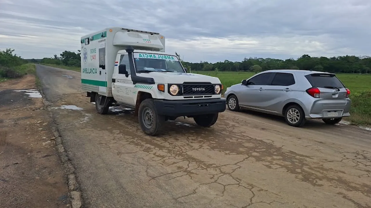 Ambulancia y automóvil circulan sobre un tramo asfaltado deteriorado con baches y grietas.
