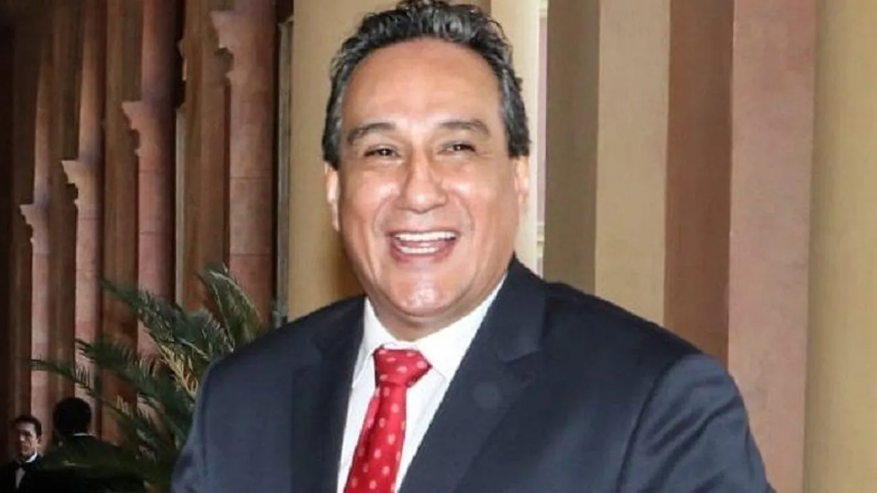 Hugo Javier González sonríe en un acto público vistiendo traje oscuro con camisa blanca y corbata roja.