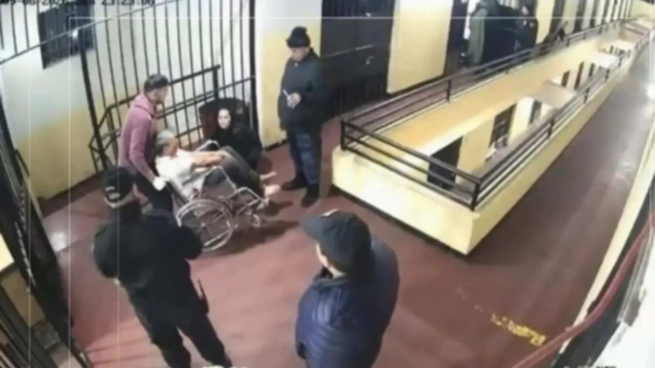 Cámara de seguridad muestra a una persona en silla de ruedas trasladada por un pasillo custodiado por varias personas.