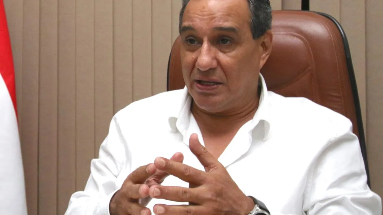 Hombre de camisa blanca gesticula con ambas manos abiertas mientras habla sentado en un sillón