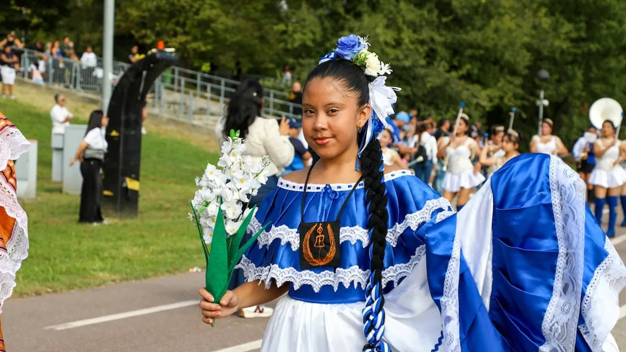 Joven vestida con traje folclórico azul y blanco sostiene un ramo de flores artificiales blancas.