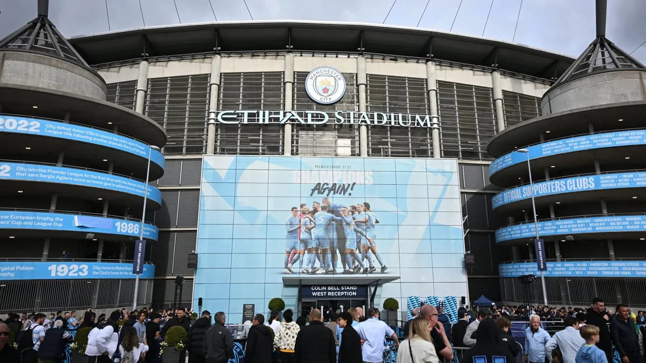 Exterior del Etihad Stadium con aficionados frente a la entrada y carteles gigantes del Manchester City.