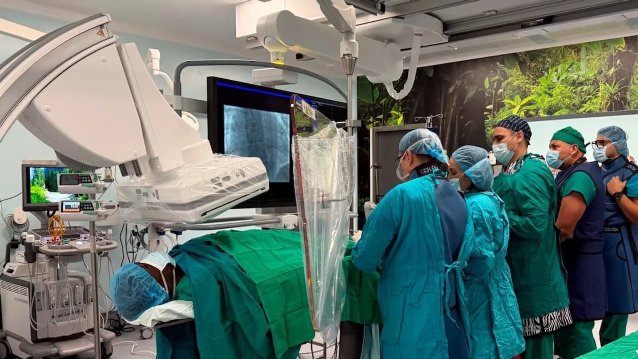 Equipo médico con vestimenta quirúrgica realiza un procedimiento complejo frente a monitores en sala de operaciones.