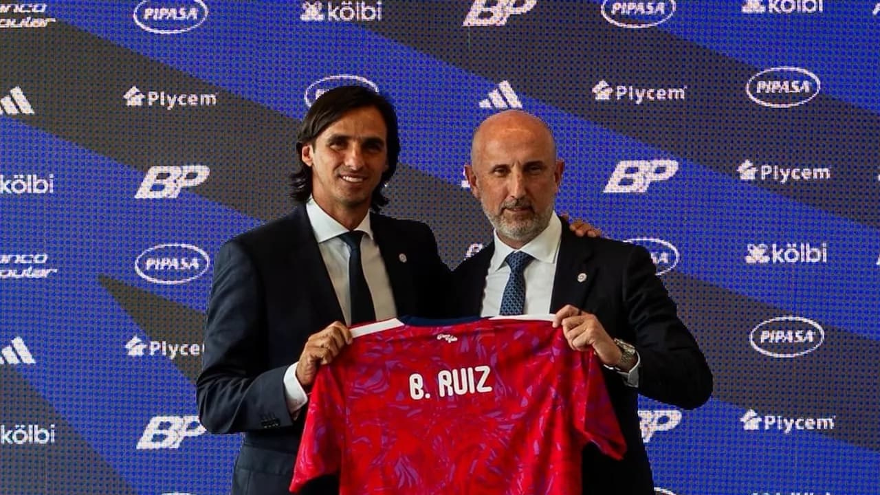 Bryan Ruiz sonríe junto a un dirigente mientras sostienen una camiseta roja con su nombre en una presentación oficial.