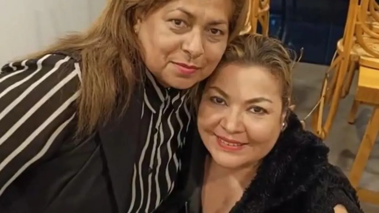 La senadora Zenaida Delgado sonríe en primer plano junto a otra mujer en un salón con sillas de madera al fondo.