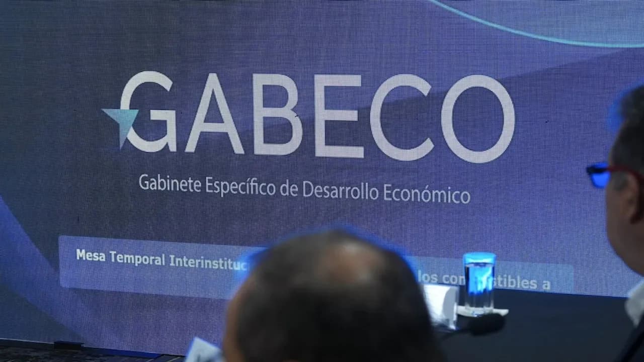Pantalla con el logo de Gabeco en una reunión gubernamental observada desde atrás por asistentes.