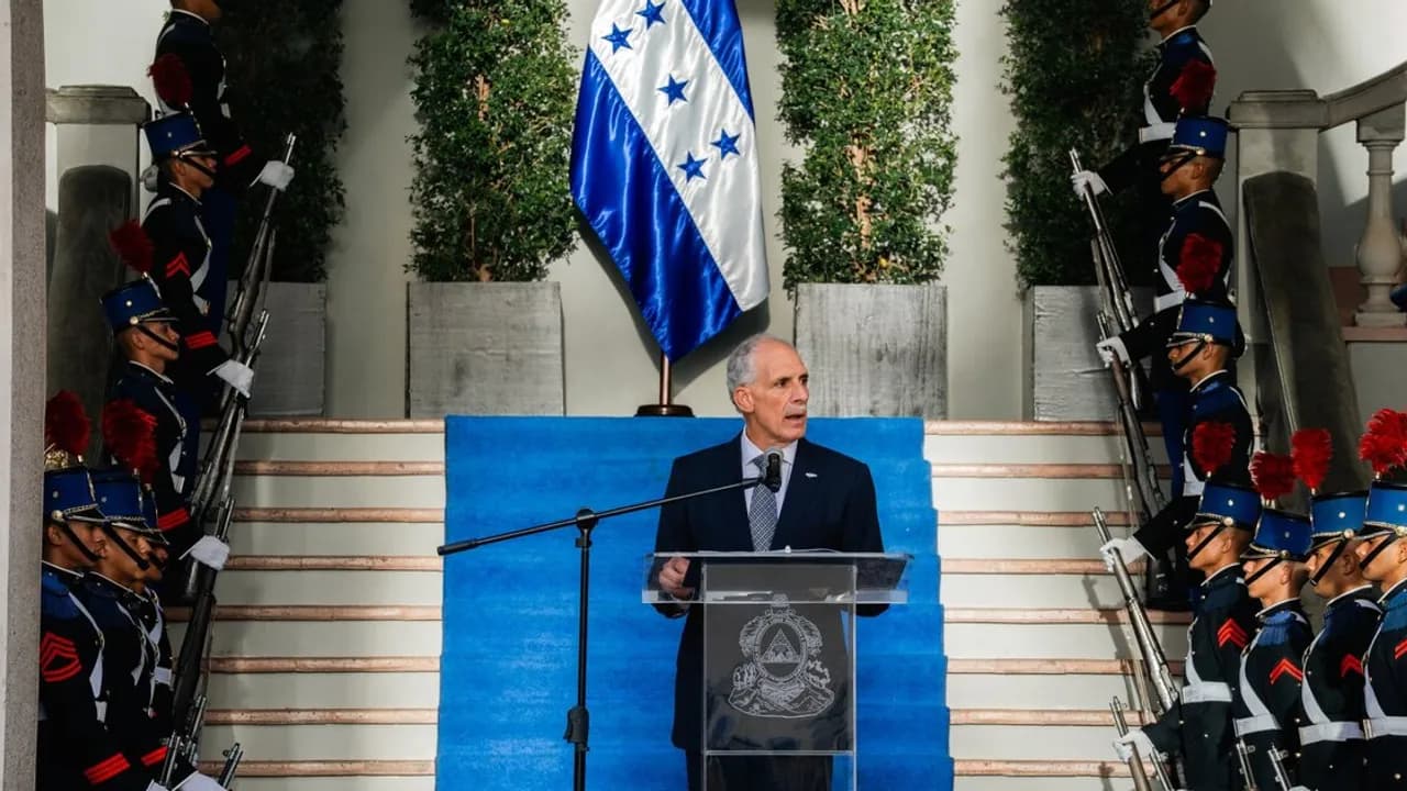 Hombre con traje formal brinda un discurso en un podio flanqueado por guardias con uniforme de gala.